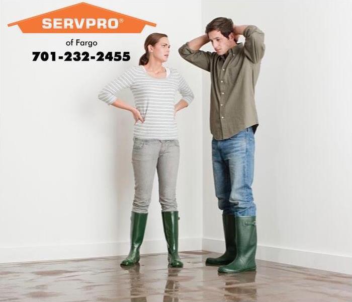  Man and woman standing on a wet floor wearing rain boots.